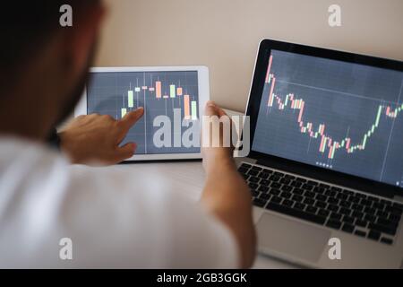 Young adult man trading on line with tablet pc connected to stock market. People, finance, investments. Over the shoulders Stock Photo