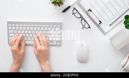 Female hands typing on keyboard at white table office workspace. Flat lay woman hands on white table desk use pc computer. Top view. Long web banner Stock Photo