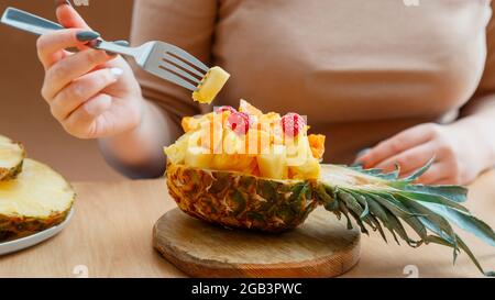 Fruit salad in half pineapple bowl. Tasty tropical fruits salad eat woman in cafe. Food fruit mix dessert served on cutting board in Pineapple. Long Stock Photo