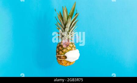 Pineapple in pink sunglasses medical mask on color blue summer background. Pineapple fruit funny face in protective mask in covid coronavirus lockdown Stock Photo
