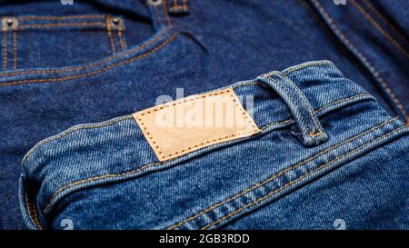Blue denim jeans with emty label. Brown blank leather label tag on denim pants background. Blank mockup beige leather label. Close up long web banner Stock Photo
