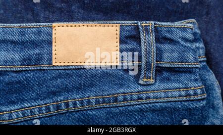Brown blank leather label tag on denim pants background. Blank
