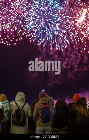 View from the back at people in wark clothes shooting fireworks on the phone at cold night. Stock Photo