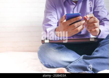 Work from home concept, unrecognized man sitting on bed working on phone  Stock Photo