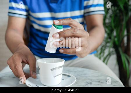 young man putting artificial sweetener in tea, Stock Photo