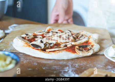 Preparing the Italian pizza known as the Margherita. Yeast dough pizza with mushrooms, mozzarella cheese and tomato sauce. Stock Photo