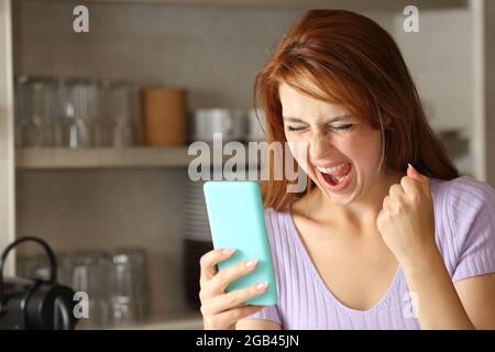 Excited woman checking smart phone content in the kitchen at home Stock Photo