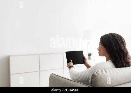 Smart home concept. Millennial woman using digital tablet with blank screen, adjusting house automation processes Stock Photo