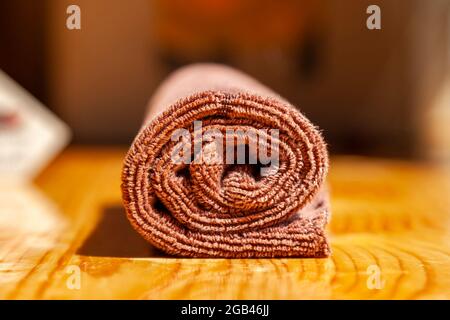 Brown three-ply microfibre tea towel rolled up on a wooden surface Stock Photo