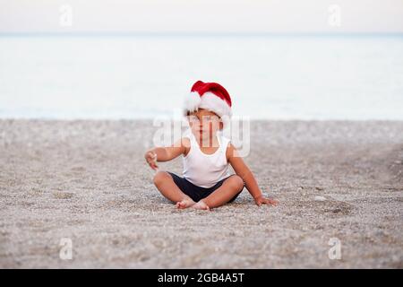 Little caucasian boy is celebrating New Year's Eve or Christmas on the beach, seaside. Holiday concept, Christmas mood. High quality photo Stock Photo