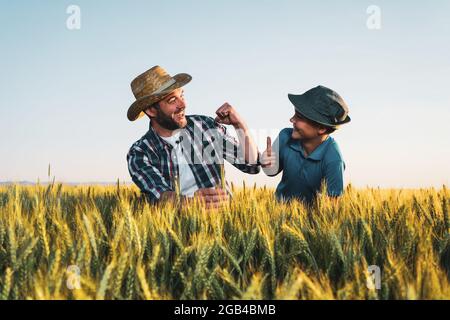 Father and son are standing in their growing wheat field. They are happy because of successful sowing. Stock Photo