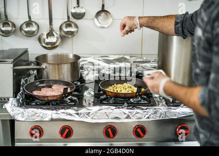 Professional cook is preparing meal in restaurant's kitchen. He is inserting spices in meal during cooking. Stock Photo