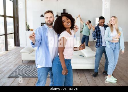 Multiracial young couple partying with their diverse friends, dancing and drinking beer at home Stock Photo
