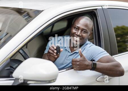 Satisfied black man sitting in nice car, showing key Stock Photo