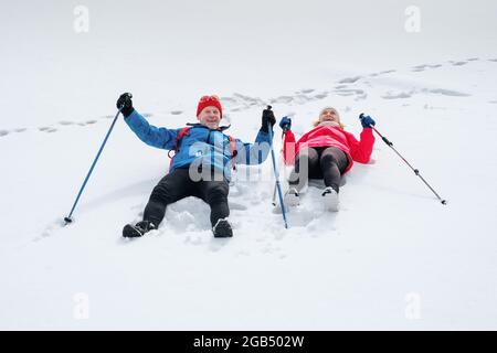 Smiling senior couple lying on snow outdoors and happy laugh. Stock Photo