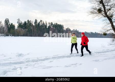 Smiling senior couple jogging in snowy winter park. Elderly wife and husband doing workout outdoors. Active lifestyle concept.