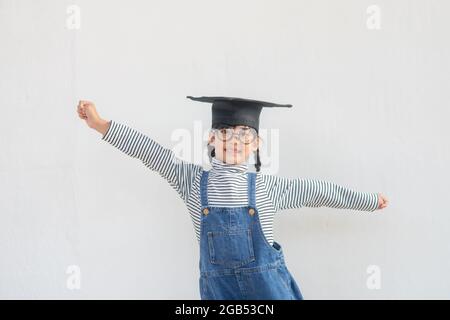 children girl wearing a graduate cap over white background very happy and excited doing winner gesture with arms raised, smiling and screaming for suc Stock Photo