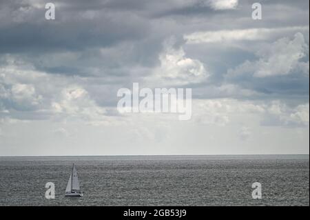 A single sail boat on the North Sea off the coast of Lowestoft, Suffolk, with storm clouds gathering about the sails Stock Photo