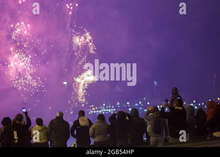 View from the back at unrecognizable people in warm clothes shooting fireworks on the phone at cold night. Stock Photo