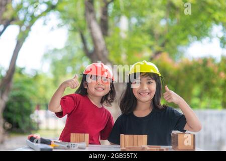 Asian Siblings girls wearing engineering hats building House from the wooden toy. To learning and enhance development, little architect. Stock Photo