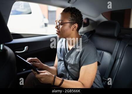 African woman sitting in back seat of the car and working online using digital tablet Stock Photo