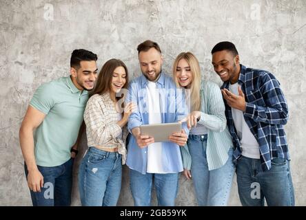 Group of millennial students using tablet together, communicating online, browsing web, studying remotely Stock Photo