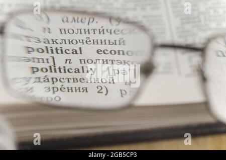 Reading glasses and an open book in close-up. Old Russian-English Dictionary. Selective Focus on the word POLITICAL ECONOMIC Stock Photo