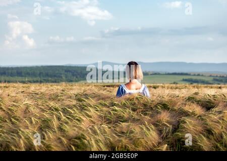 Woman in a wheat field on the background of the blue sky with clouds Stock Photo