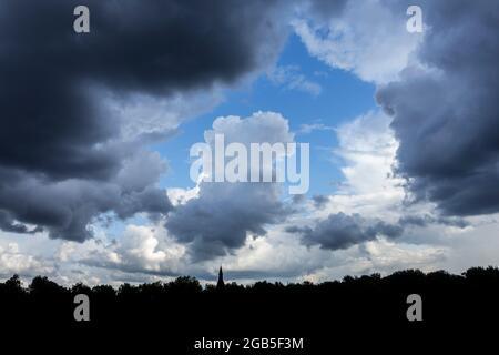 Gap in white and grey cumulus clouds showing patch of blue sky on a rainy day in summer Stock Photo