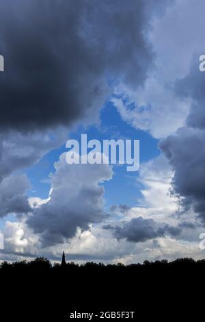 Gap in white and grey cumulus clouds showing patch of blue sky on a rainy day in summer Stock Photo