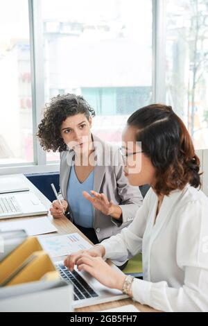 Frowning emotional businesswoman talking to her colleague who does too many mistakes in reports and documents Stock Photo