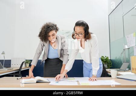 Serious businesswomen bending over table with charts and reports and analyzing financial data Stock Photo
