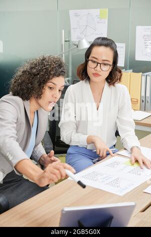 Young female entrepreneurs working with reports, analyzing statisctics on tablet computer and pronted documents Stock Photo