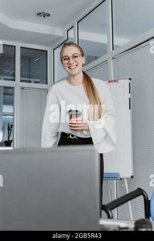Remote Meetings, Video Conferencing. Young business woman drinking coffee and communicating with colleagues via video call on laptop in the office Stock Photo