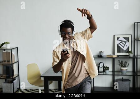 African happy man in headphones using his mobile phone to listen to music and dancing at home Stock Photo