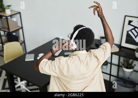 Rear view of African man listening to music in wireless headphones and dancing at offices Stock Photo