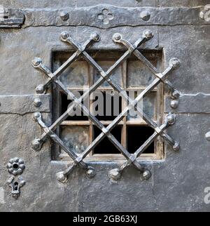 Old window behind metal grate in medieval door Stock Photo