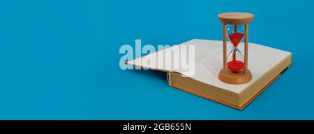 hourglass and book on blue on blue panorama background Stock Photo
