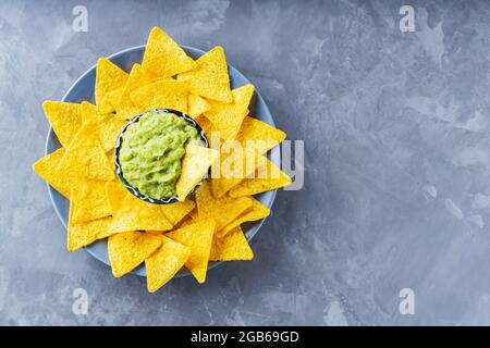 Mexican sauce guacamole with nachos chips in a plate. Bowl of guacamole with nachos chips on a gray background. Copy space. Flat lay Stock Photo