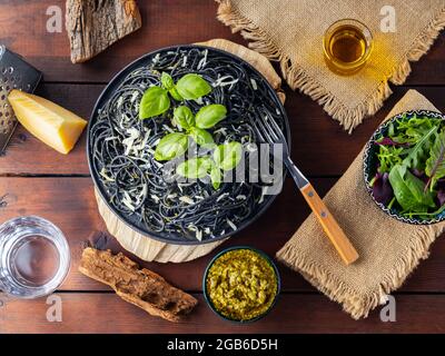 Pasta spaghetti with parmesan cheese, basil and pesto sauce. Black pasta, sauce pesto and fresh mix salad of greens on wooden boards. Flat lay. Top vi Stock Photo