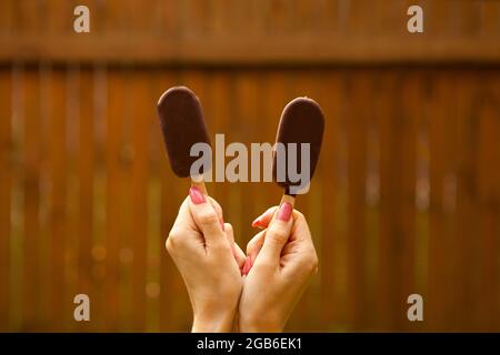 summer sweet food. female hands holding two chocolate ice cream on brown background Stock Photo