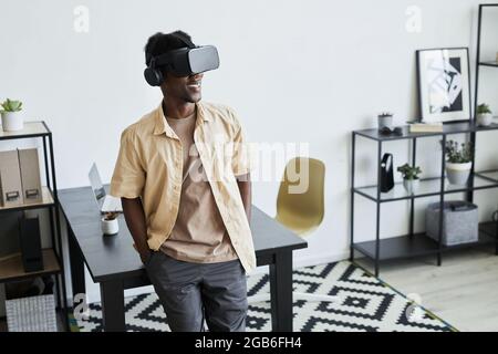 African young businessman in virtual reality glasses working online while standing at office Stock Photo