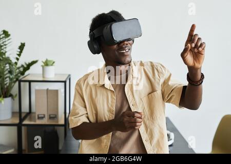 African smiling man gesturing while standing in the room, he playing in virtual reality game Stock Photo