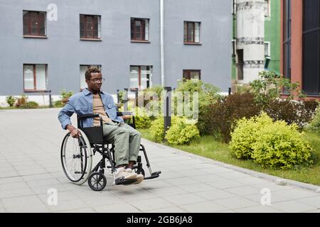 Serious handicapped young African-American man in eyeglasses sitting in wheelchair outdoors Stock Photo