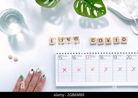 Text Long Covid, wooden letters. Hand with weekly planner, calendar with all days crossed out. Cancellation, change of plans, chronic covid illness Stock Photo