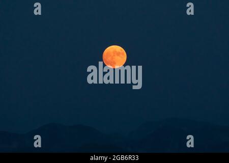 Splendid full red moon rises over the mountain ridges of the Apennines. Stock Photo