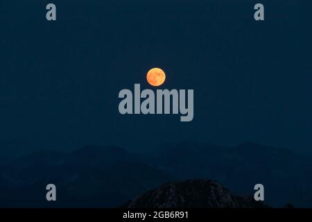 Splendid full red moon rises over the mountain ridges of the Apennines. Stock Photo