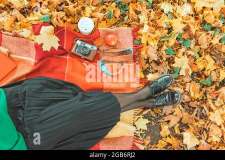 women resting at blanket on the ground in yellow autumn leaves. cup of coffee red apple and a book. no face Stock Photo