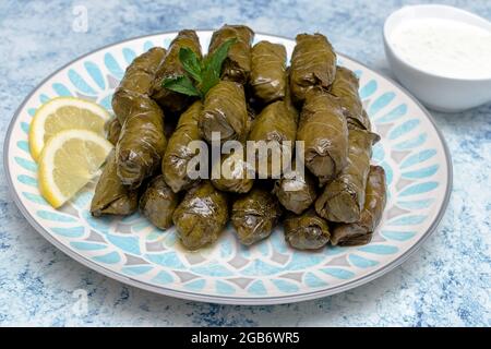 Traditional Bulgarian homemade stuffed vine leaves with rice and garnished with fresh tomatoes, lemon and sauce of yogurt Stock Photo