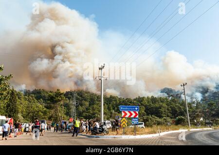 Marmaris, Mugla, Turkey – August 1, 2021. Smoke from a forest fire rising over Hisaronu neighbourhood of Marmaris resort town of Turkey on August 1, 2021. View with people and cars. Stock Photo